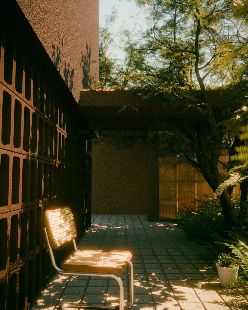 A serene patio featuring a single chair under soft sunlight surrounded by lush greenery.