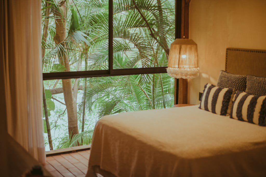 Cozy modern bedroom with a window overlooking tropical vegetation, creating a serene ambiance.