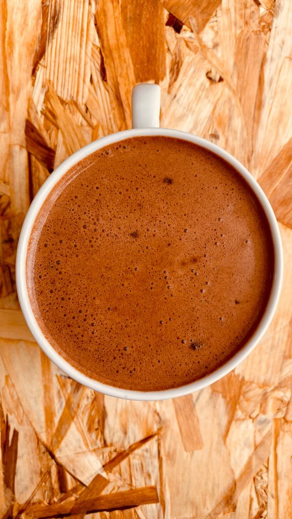 Top view of a creamy hot chocolate in a white mug on a wooden background. Warm and inviting.